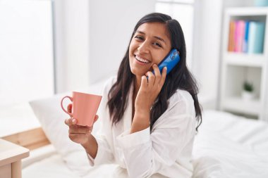 Genç, güzel, İspanyol bir kadın. Akıllı telefondan konuşuyor. Yatak odasında kahve içiyor.