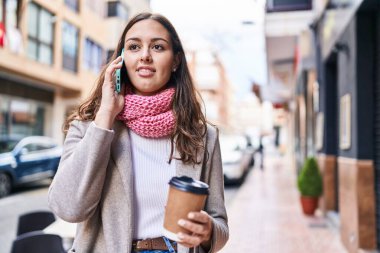 Young beautiful hispanic woman using smartphone drinking coffee at street