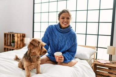 Genç, güzel, İspanyol bir kadın. Bir fincan kahve içiyor. Yatakta köpekle oturuyor.