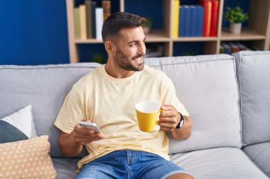 Genç İspanyol adam akıllı telefon kullanıyor. Evde kahve içiyor.