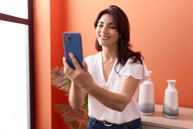 Orta yaşlı İspanyol kadın evde akıllı telefon kullanıyor.