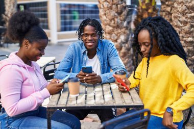 Afro-Amerikalı arkadaşlar akıllı telefon kullanıyor kahve içiyor kahve dükkanının terasında bankta oturuyor.