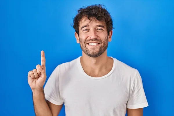 西班牙裔年轻人站在蓝色的背景上 带着第一指尖 面带微笑 自信而快乐 — 图库照片