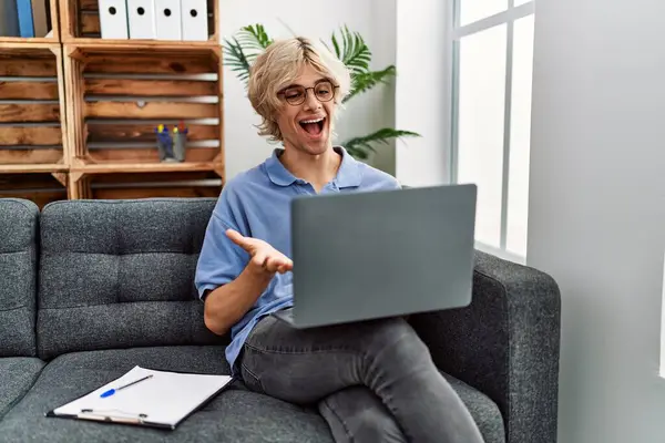 幸せな笑顔で達成を祝うソファの上に座ってコンピュータのラップトップを使用して作業している若い男と勝者式とともに上げ手 — ストック写真