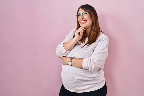 怀孕妇女手托着下巴站在粉红的背景上思考着问题 沉思着 微笑和体贴的脸 怀疑概念 — 图库照片