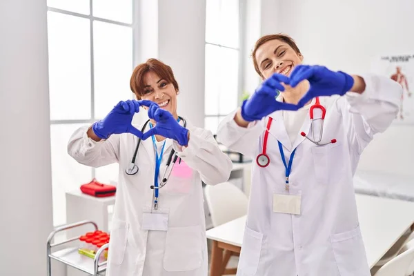 两个穿着医生制服和听诊器的女人带着爱意微笑 用手表现出心脏的符号和形体 浪漫的概念 — 图库照片