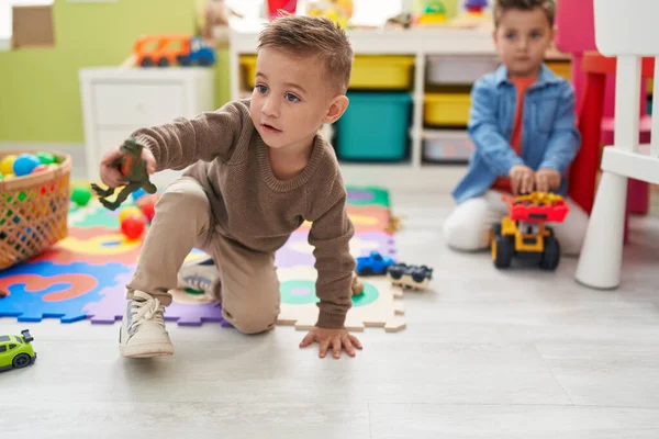 幼稚園の床に座っているトラクターや恐竜のおもちゃで遊んでいる愛らしい男の子 — ストック写真