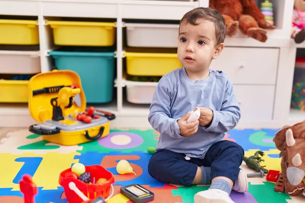 他那可爱的惊慌失措的孩子坐在幼儿园的地板上玩超级市场游戏 — 图库照片