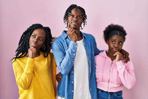 一组三个年轻的黑人站在粉红的背景上手托着下巴思考着问题 沉思着表情 脸上挂着沉思的笑容 怀疑概念 — 图库照片
