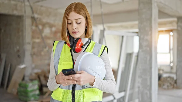 年轻的金发女建筑师在建筑工地用智能手机顶着硬礼帽 — 图库照片
