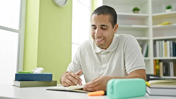 Young hispanic man student reading book at library university