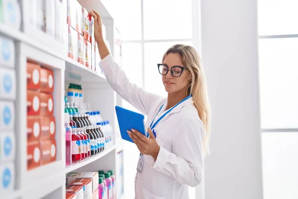 薬局で棚に製品を保持タッチパッドを使用して若いブロンドの女性薬剤師 — ストック写真
