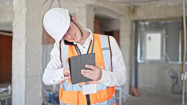 年轻的高加索人建筑师在建筑工地用触摸板用智能手机交谈 — 图库照片