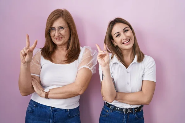 西班牙裔母亲和女儿穿着宽松的白色T恤 背景是粉色的 高兴地微笑着 用手指在镜头前眨眼示意胜利 第二点 — 图库照片