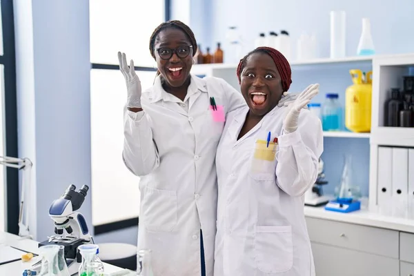 幸せな笑顔で勝利を祝う科学研究所で働く2人のアフリカ人女性と手を挙げて勝者の表情 — ストック写真