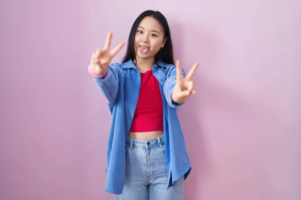 Młoda Azjatka Stojąca Nad Różowym Tłem Uśmiechnięta Językiem Pokazująca Palce — Zdjęcie stockowe