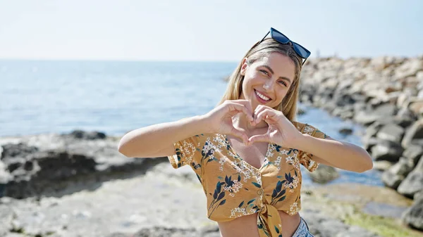 Joven Mujer Rubia Sonriendo Confiado Haciendo Gesto Corazón Playa — Foto de Stock