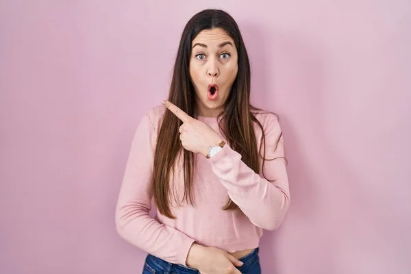 Jonge Brunette Vrouw Staande Roze Achtergrond Verrast Wijzend Met Vinger — Stockfoto