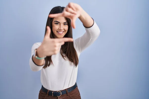 Young Brunette Woman Standing Blue Background Smiling Making Frame Hands — Stok fotoğraf