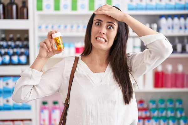 若いですブルネット女性ショッピングで薬局ドラッグストア保持薬を強調し フラストレーションとともに手で頭 驚きと怒っている顔 — ストック写真