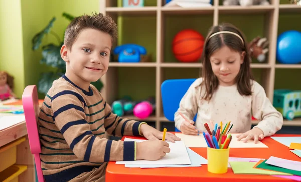 幼稚園の机に座って紙絵を描く大人の男の子と女の子 — ストック写真