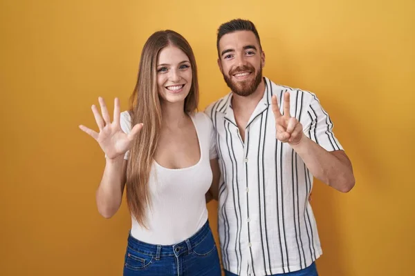 Sarı Arka Planda Duran Genç Çift Yedinci Parmaklarını Gösterip Işaret — Stok fotoğraf