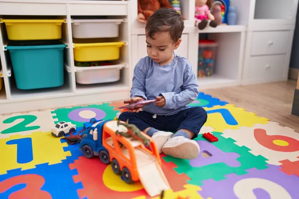 幼稚園の床に座っている車や恐竜のおもちゃで遊んでいる愛らしいヒスパニック少年 — ストック写真