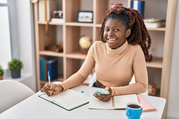 Afroamerykanka Student Pomocą Smartfona Pisanie Notatniku Domu — Zdjęcie stockowe