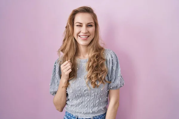 stock image Beautiful blonde woman standing over pink background winking looking at the camera with sexy expression, cheerful and happy face. 