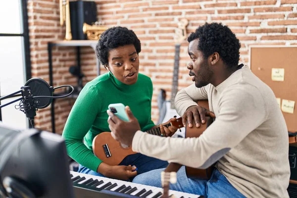 Afrika kökenli Amerikalı erkek ve kadın müzik grubu müzik stüdyosunda ukelele çalarken akıllı telefon kullanıyor.