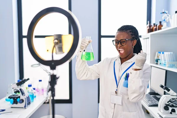 科学研究所で働いているアフリカの女性は 誇りを持って叫んでスマートフォンでチュートリアルを行う 勝利と成功を祝う非常に腕を上げ興奮して — ストック写真
