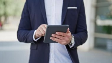 Sokakta dokunmatik ped kullanan genç Latin iş adamı gülümsüyor.