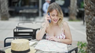 Genç sarışın kadın turist görünümlü şehir haritası kahve dükkanının terasında akıllı telefondan konuşuyor.