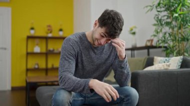 Kanepede oturan Latin asıllı genç bir adam. Şüpheli bir ifadeyle.