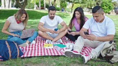 Bir grup öğrenci parkta bilgisayar ve akıllı telefonlar kullanıyor.