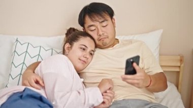 Yatakta uzanan erkek ve kadın yatak odasında akıllı telefondan selfie çekiyorlar.