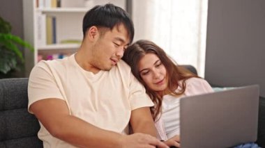 Man and woman couple sitting on sofa using laptop at home