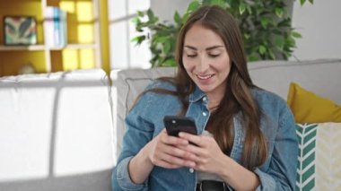 Evdeki kanepede oturan akıllı telefon kullanan genç, güzel İspanyol kadın.