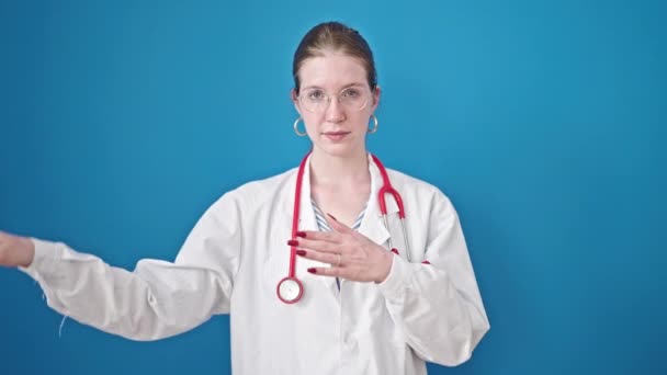 若いですブロンド女性医師作り誓いとともに手上の胸上の隔離された青の背景 — ストック動画