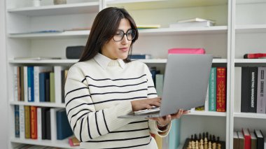 Kütüphanede dizüstü bilgisayar kullanan güzel İspanyol bir kız öğrenci.