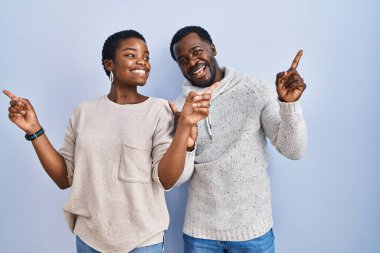 Mavi arka planda dikilen genç Afro-Amerikan çift parmaklarını farklı yönlere çevirerek gülümsüyor. reklam için kopyalama alanı 