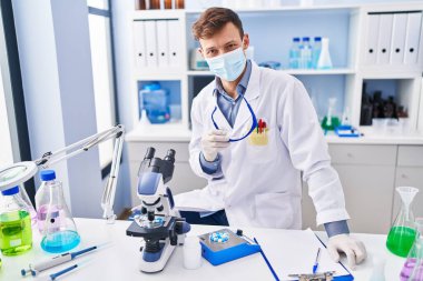 Young man scientist wearing medical mask sitting on table at laboratory