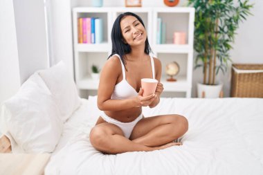 Young beautiful latin woman wearing lingerie drinking coffee at bedroom