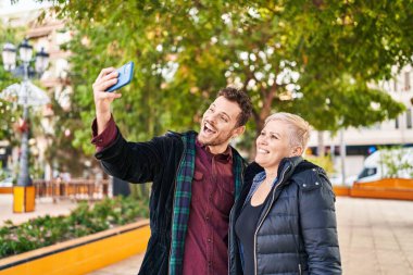 Anne ve oğul parktaki akıllı telefonun yanında özçekim yaparken gülümsüyor.