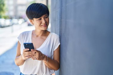 Middle age chinese woman smiling confident using smartphone at street