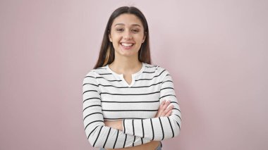 Young beautiful hispanic woman smiling confident standing with arms crossed gesture over isolated pink background