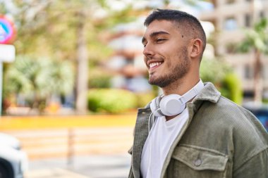 Parkta kulaklık takıp gülümseyen İspanyol genç adam.