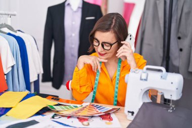 Orta yaşlı kadın terzi akıllı telefondan konuşuyor. Terzi dükkanında renk testi yapıyorlar.