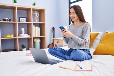 Genç, güzel İspanyol kız öğrenci. Yatak odasında akıllı telefon kullanıyor.