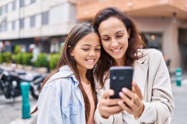 Woman and girl mother and daughter using smartphone at street